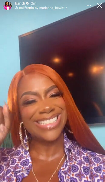 Kandi smiling in a purple patterned top with straight, auburn red, hair.