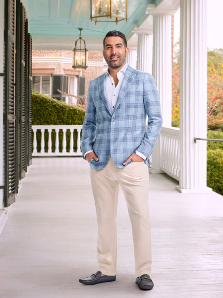 Rod in a blue, patterned, blazer and beige pants on a porch.
