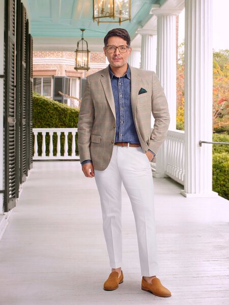 Rodrigo wearing a beige blazer, blue button down shirt, and white pants on a porch.
