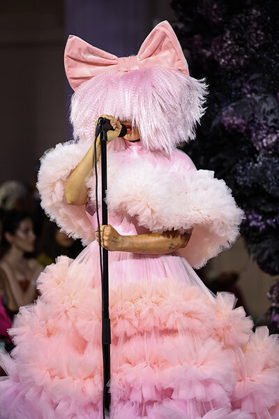 Sia performs wearing a multi-tiered, pink outfit, with pink hair, and a large pink bow.