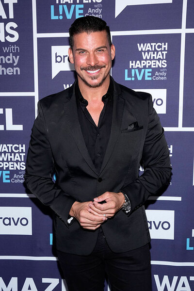 Jax Taylor smiling in an all black suit on the WWHL step and repeat.