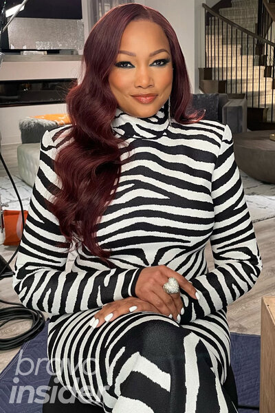 Garcelle Beauvais seated wearing a zebra print, fitted, dress.