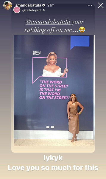 Gizelle Bryant barefoot standing in front of a photo of herself.