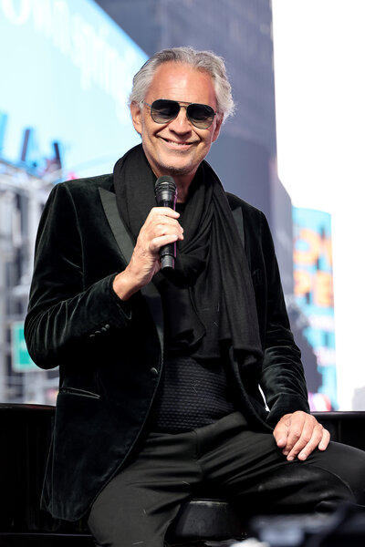 Andrea Bocelli sitting on stage during a performance in a black outfit.