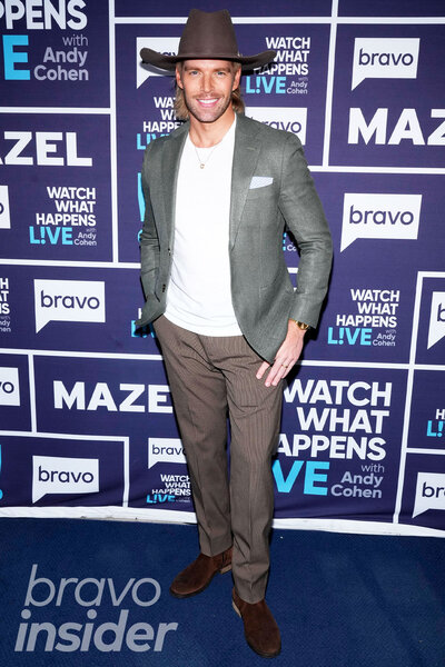 Kyle Cooke wearing an earth-toned suit and hat in front of a step and repeat at the Watch What Happens Live clubhouse in New York City.