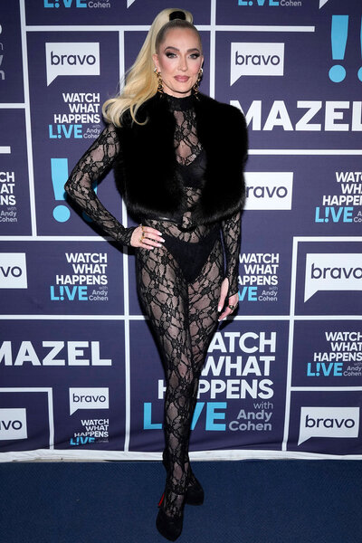 Erika Jayne in a sheer jumpsuit standing in front of the Watch What Happens Live step and repeat.