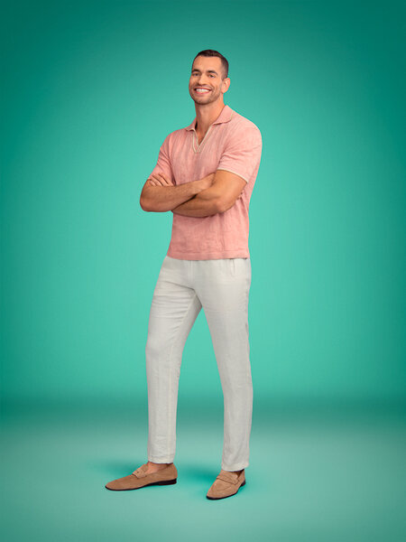 Full length of Jesse Solomon wearing a pink polo and cream slacks in front of a green backdrop
