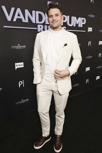 Tom Schwartz wearing a white suit in front of a step and repeat.