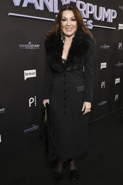 Lisa Vanderpump in a black coat in front of a step and repeat.