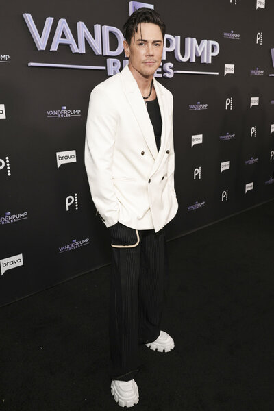 Tom Sandoval in a white and black outfit in front of a step and repeat.