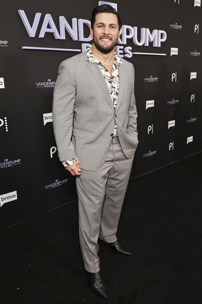 Brock Davies wearing a grey suit in front of a step and repeat.