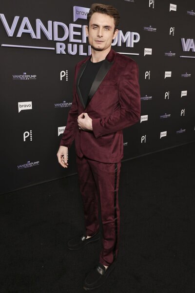 James Kennedy wearing a red velvet suit in front of a step and repeat.