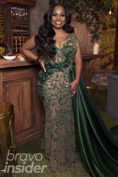 Heavenly Kimes wearing a jewel-encrusted, green, sheer gown in front of a vineyard-inspired set.