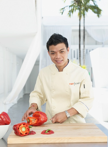 Hung Huynh wearing a chefs coat and slicing vegetables