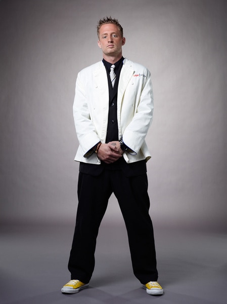 Full Length of Michael Voltaggio wearing his chef's jacket and black pants in front of a grey backdrop