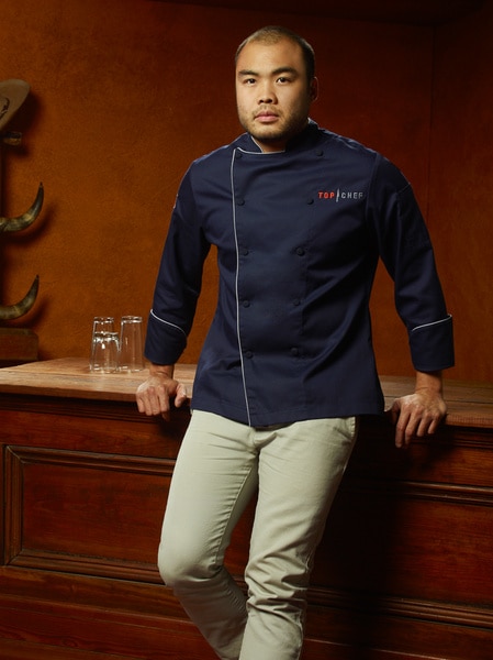 Paul Qui wearing his chef's jacket while leaning on a wood bar.