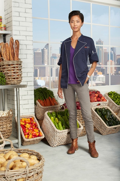 Full length of Kristen Kish wearing her chef's jacket in a vegetable pantry.