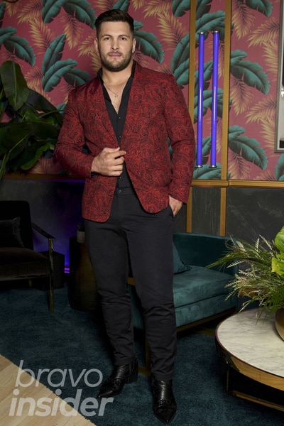 Brock Davies wearing a red blazer in front a patterned wall.