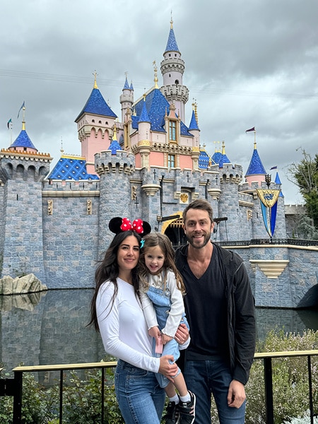 Michelle Lally, Isabelle Lally, and Aaron Nosler posing together in front of a Disney castle.