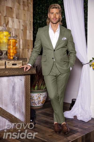 Kyle Cooke posing and wearing an olive suit in front of a themed set.