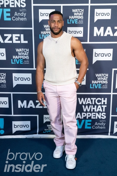 Full length of Amir Lancaster wearing a white top and pink pants in front of the Watch What Happens step and repeat