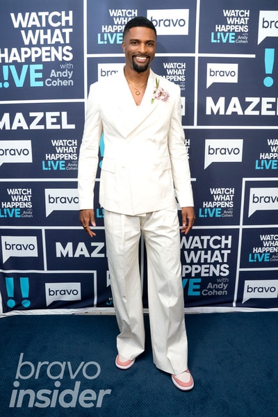 Full length of Alex Tyree wearing a white suit in front of the Watch What Happens step and repeat
