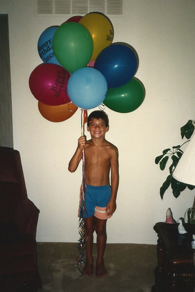 Jax Taylor holds a bunch of balloons while smiling.