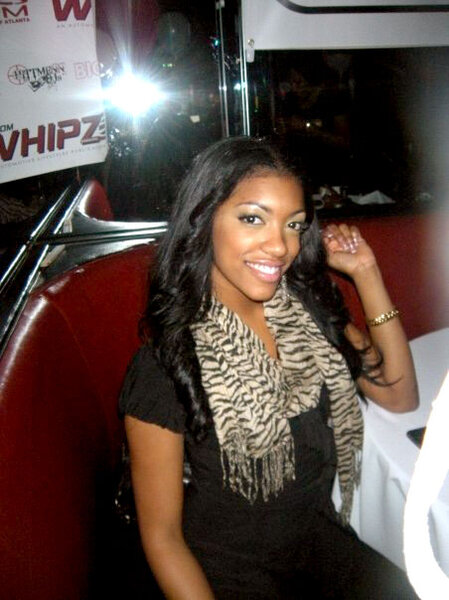 Porsha Williams sitting in a booth wearing a black top and an animal print scarf