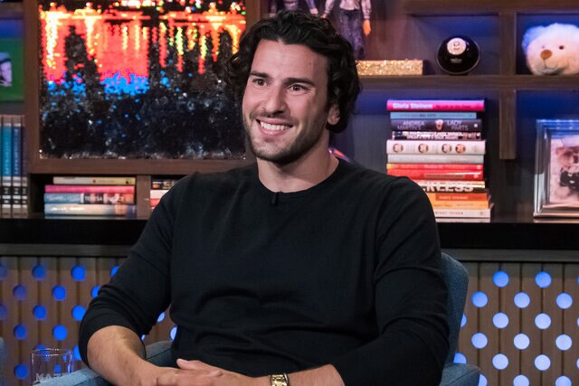 Steve smiling with long hair in a black sweater at the WWHL clubhouse.
