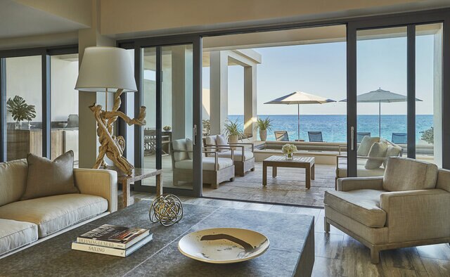 An indoor seating area with a terrace and a private pool and lounge chairs and umbrellas overlooking the ocean.