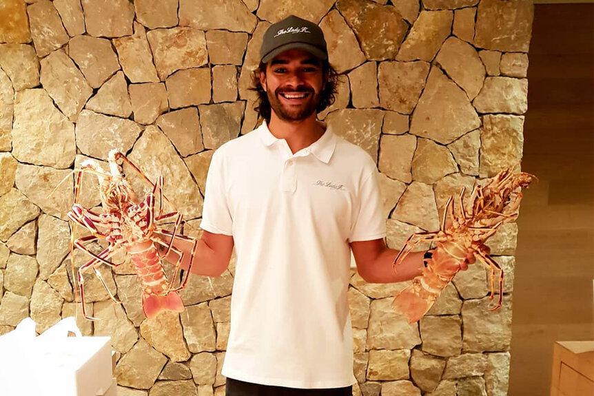 Hindrigo Kiko Lorran smiling in front of a stone wall while holding fresh lobsters.