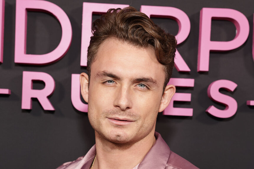 James Kennedy in front of a step and repeat at an event wearing a pink, collared, shirt.
