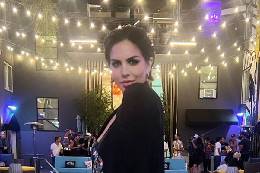 Katie Maloney posing in an all black outfit in front of a pool and string lights.