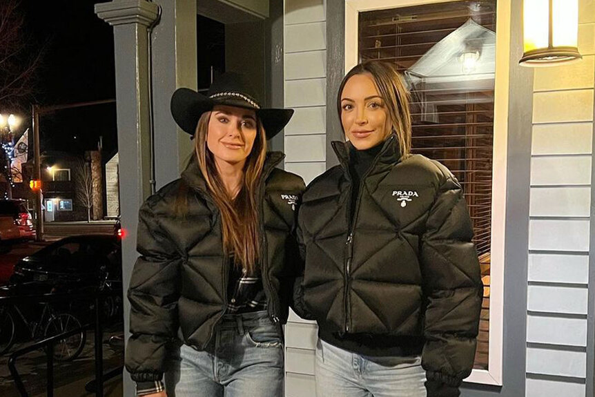 Kyle and Farrah pose together in matching, black, Prada puffer jackets in front of a building.