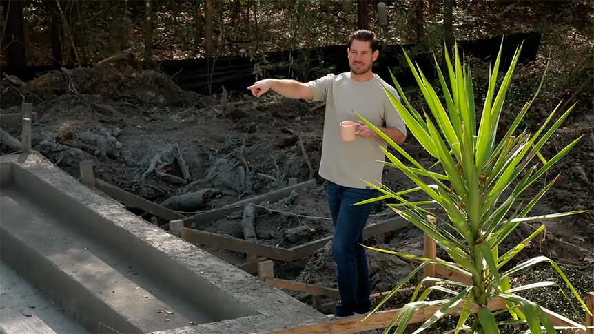 Craig Conover standing and pointing to the pool being installed in his backyard.