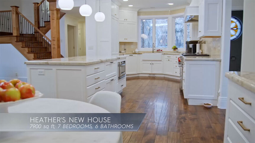 Heather Gay's all-white kitchen with wood flooring and with text overlaid, "Heather's New House; 7900 sq. ft; 7 bedrooms, 6 bathrooms."