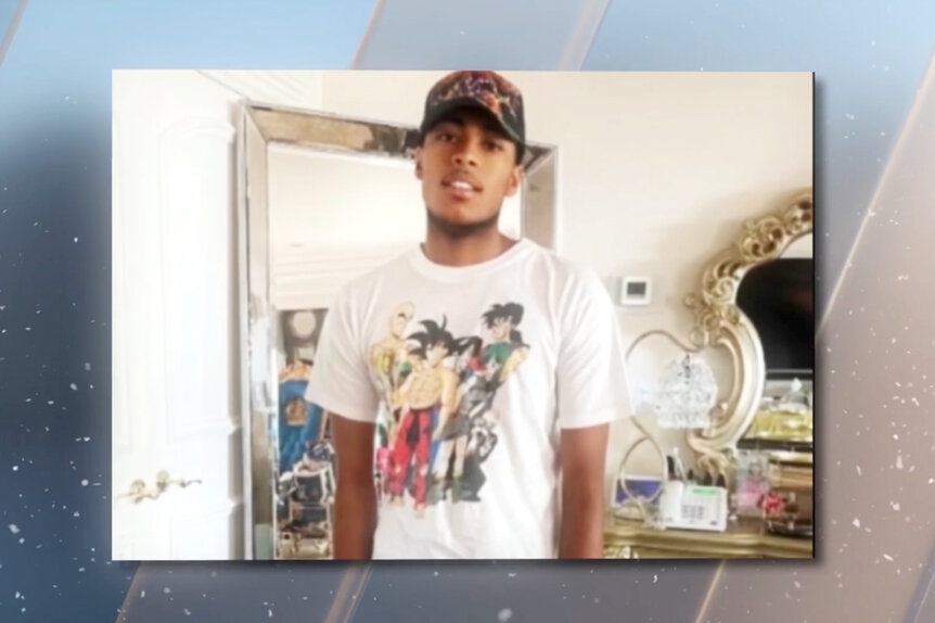 Robert Cosby Jr. wearing a white tee shirt and a black hat in a bedroom.