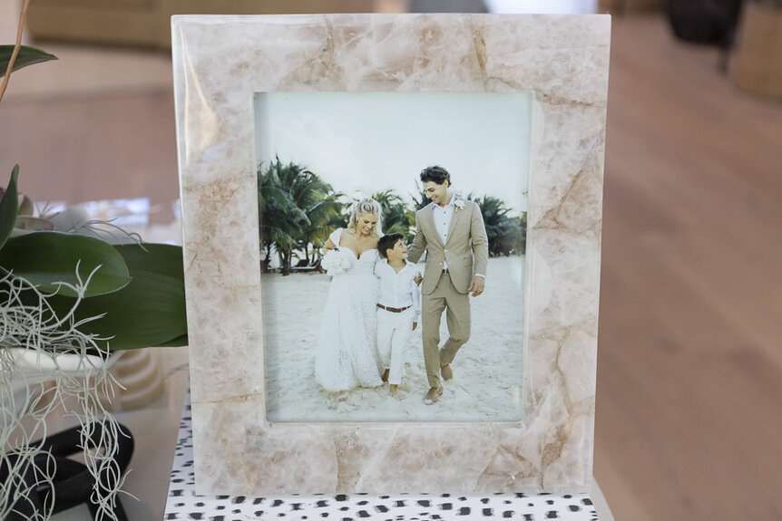 A marble framed photo of Madison LeCroy, Hudson Hughes, and Brett Randle at their wedding party in Charleston, South Carolina.