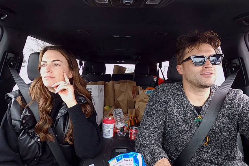 Tom Schwartz driving a car and Katie Flood in the passenger seat.