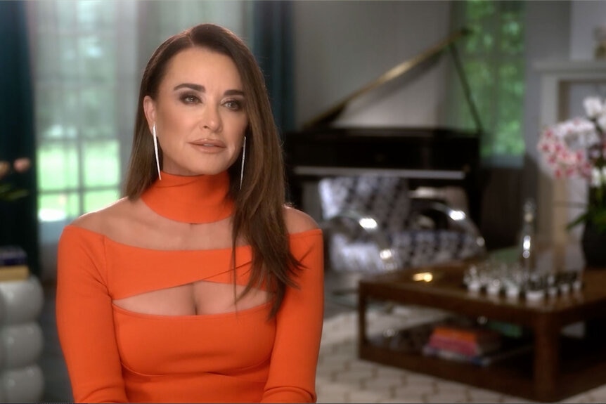 Kyle Richards wears an orange dress during her Real Housewives of Beverly Hills confessional