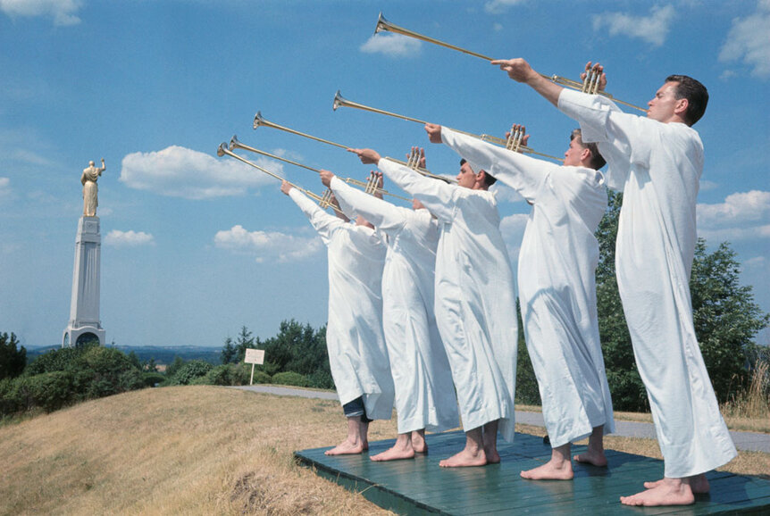 Five men playing trumpets in white ribes during a Mormon religeous festival.