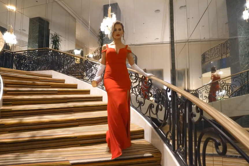 Dorit Kemsley walks down a set of spiral stairs while wearing a long red dress
