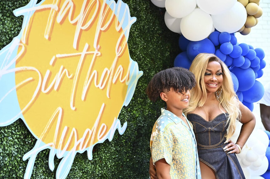 Phaedra Parks and Ayden Nida standing in front of a birthday photo wall.