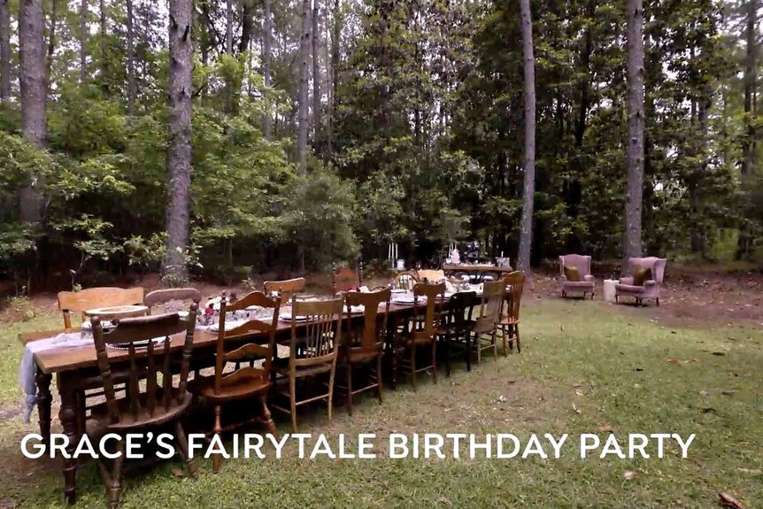 A long decorated table with chairs sits near a forest.