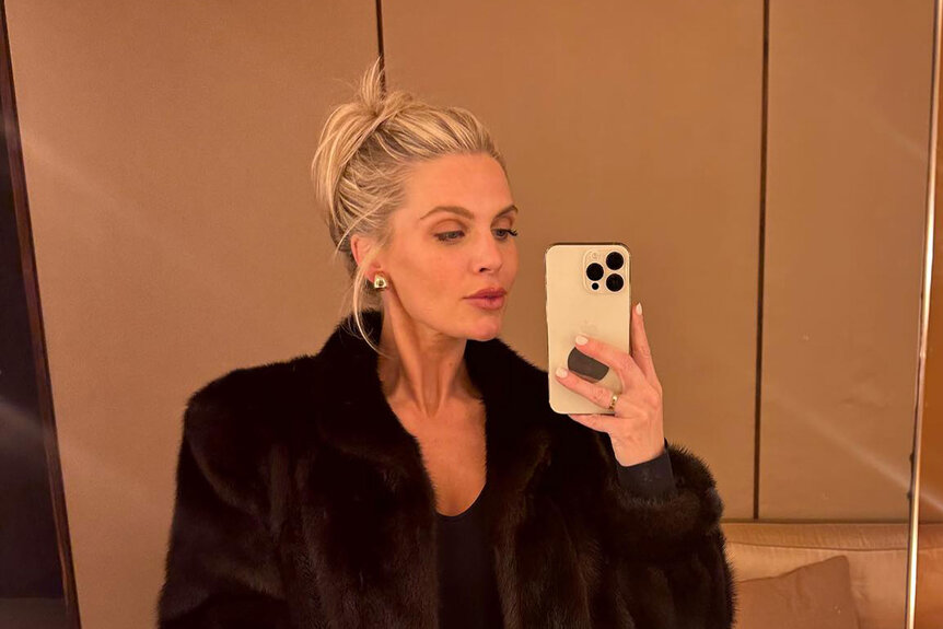 Madison LeCroy wearing a fur coat standing in front of the mirror.