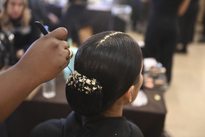 Gold foil being placed onto a model's bun by a hairstylist.