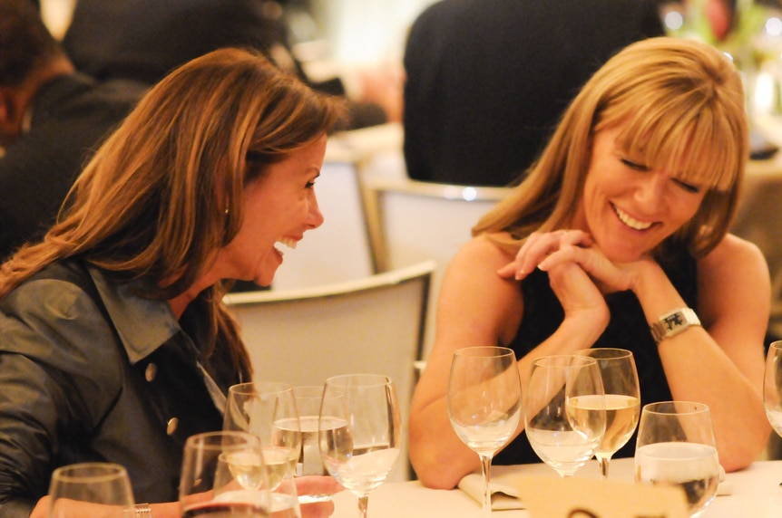 Lynda Erkiletian and Mary Amons smiling and laughing at a dinner table.