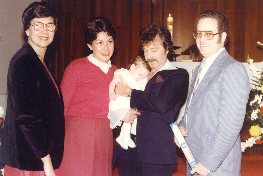 Lisa Hochstein as a baby being held by her parents at her christening.