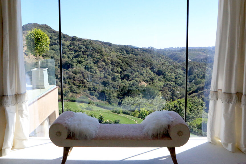 A bench in front of a window with a view of the Los Angeles hills.