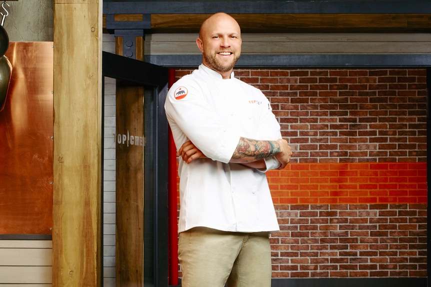Jeremy Ford wearing his chef's jacket in front of a brick wall.
